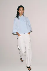 Camisa Zara Woman Collection de algodón con estampado de rayas verticales blancas y celestes. Presenta cuello perkins, mangas tres cuartos y un diseño asimétrico con cierre frontal cruzado mediante botones.