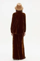 Pantalón de terciopelo color marrón oscuro con textura brillante y pierna ancha. Presenta tiro medio-alto con elástico en la espalda y corte limpio en el delantero.