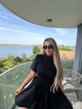 Vestido corto negro con cuerpo superior fruncido, cuello alto y mangas cortas amplias. La falda presenta un diseño acampanado con mucho vuelo.