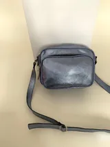 Bandolera rectangular de cuero azul metalizado con correa larga regulable. Cuenta con un bolsillo frontal con fuelle y un bolsillo trasero con cierre.