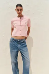 Chaqueta de punto color amarillo pálido, con cuello redondo, manga corta, cierre frontal con botones dorados y bolsillos de parche en el pecho.