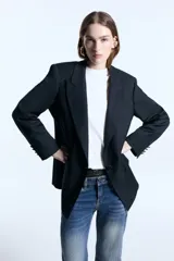 Blazer oversize de sarga color negro, con hombreras marcadas, frente con terminación en punta y cierre de un botón forrado. Posee dos bolsillos frontales con detalle de logo en hotfix y bordado en el cuello trasero. Totalmente forrado.