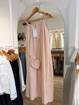 Vestido midi rosado de silueta amplia y fluida, con tirantes finos ajustables y escote fruncido. Incluye una pequeña cartera haciendo juego con cordones y cuentas decorativas.