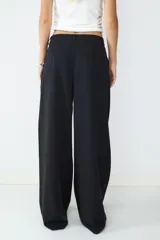 Pantalón de vestir negro de tiro alto con pliegues frontales, corte amplio y pernera recta. Cuenta con bolsillos laterales y cierre frontal con cremallera y botón.
