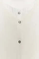 Chaqueta efecto doble de punto color beige con cuello redondo, manga por debajo del codo y cierre frontal con botones. Detalle de cuello y bajo de camisa interior asomados.