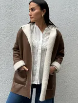 Tapado de eco cuero gamuzado color marrón con interior y bordes de corderito sintético color crema. Presenta diseño con capucha, bolsillos frontales y corte relajado.