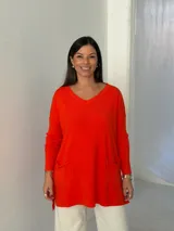 Sweater de punto color naranja, con cuello en V, manga larga y diseño holgado con bolsillos frontales y tajos laterales.
