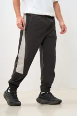 Pantalón de jogging gris oscuro con banda lateral gris claro, cintura elástica con cordón ajustable, bolsillos laterales con cierre y puños elásticos.