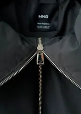 Chaqueta acolchada de corte oversize en color gris oscuro, con cuello alto estructurado, cierre frontal de cremallera metálica y bolsillos laterales.
