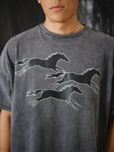Remera oversize gris con efecto stone wash y estampado en serigrafía de caballos galopando con diseño pixelado.
