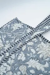 Bolso tipo tote bag de tela acolchada con estampado floral en tonos gris y blanco. Presenta asas largas reforzadas con detalle de rayas en los bordes.