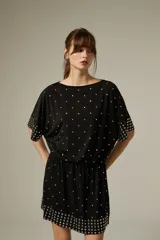 Vestido corto de poliéster color negro con escote a la base, mangas cortas y diseño holgado. Cuenta con detalles de tachas metálicas plateadas distribuidas por la prenda y agrupadas en el dobladillo y los puños.
