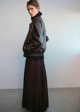 Chaqueta estilo bomber de cuero sintético en color marrón oscuro, con cuello camisero, cierre frontal de cremallera y botones a presión, bolsillos de parche con solapa y bajo elástico.