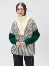 Pullover de tejido acanalado grueso con diseño a rayas verticales en color crema y negro. Presenta cuello alto con cierre frontal, mangas largas en color verde y un ajuste holgado.