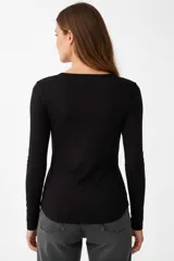 Remera blanca de manga larga, entallada, con cuello redondo y una hilera de botones en el frente. Incluye un pequeño bolsillo decorativo en el pecho.