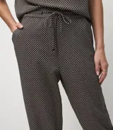Pantalón de corte sastre y estilo fluido, confeccionado en crepé con estampado pied-de-poule. Presenta cintura elástica con cordón de ajuste y bolsillos laterales.
