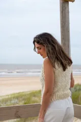 Chaleco tejido de punto en color crudo, con cuello alto y diseño sin mangas. Presenta una textura de punto grueso y corte recto.