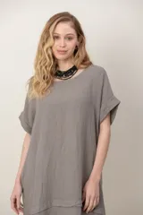 Vestido midi de lino color beige, de corte holgado y silueta acampanada. Cuenta con cuello redondo, mangas cortas amplias, bolsillos laterales y detalles de recortes horizontales en la falda con terminación asimétrica más larga en la parte trasera.