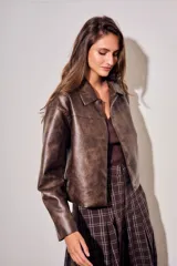 Campera de cuero vegano en tono marrón con acabado desgastado, corte recto y cierre frontal con botones a presión. Presenta cuello clásico y diseño minimalista.