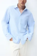 Camisa de algodón Oxford con cuello americano, bolsillo frontal y mangas largas con puños abotonados. Presenta un corte estándar y bajo redondeado.