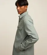 Camisa de manga larga confeccionada en sarga de algodón color verde menta, con cuello inglés y cierre frontal de botones negros. Presenta dos bolsillos de parche con solapa en el pecho y puños con botones.