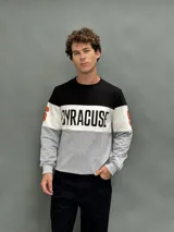 Buzo de cuello redondo con diseño de bloques de color en negro, blanco y gris. Presenta la palabra 'SYRACUSE' estampada en el frente y detalles en naranja en las mangas.