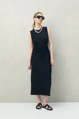 Vestido largo de punto color negro, sin mangas, con diseño entallado y un lazo lateral que permite ajustar la cintura.