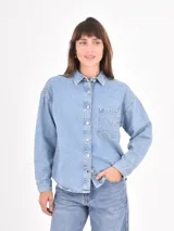 Camisa de jean de corte oversize, con cierre frontal de botones metálicos, cuello clásico y bolsillo frontal decorado con tachas plateadas.