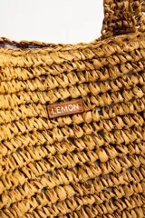 Bolso tipo tote color camel, confeccionado en material trenzado con textura rústica, doble asa de hombro y pequeño aplique metálico con el logo de la marca.