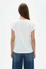 Remera de algodón blanca de manga corta, con cuello redondo y estampado frontal con la leyenda "New York" y flores abstractas en tonos marrones y rosados.