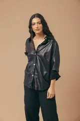 Camisa de cuero negra, de corte holgado, con cuello camisero, cierre frontal con botones y mangas largas con puños abotonados.