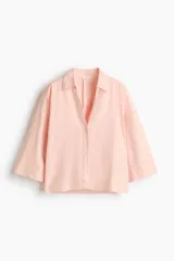 Camisa de corte holgado confeccionada en mezcla de lino y viscosa, de color rosado. Presenta cuello abierto, cierre frontal con botones, hombros caídos y mangas tres cuartos.