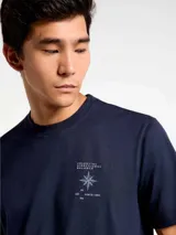 Camiseta blanca de algodón con cuello redondo y mangas cortas. Estampa rectangular con borde negro que contiene la frase "NATURAL ATMOSPHERE" en letras mayúsculas y una imagen de montañas y mar.