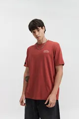 Remera de manga corta color terracota con estampado frontal blanco que dice "MISTRAL Architecture of Reality REG. TM / EST. 76". Tiene un fit regular y está confeccionada en algodón.