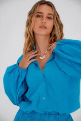 Conjunto de lino compuesto por una camisa de mangas abullonadas con puños elásticos y un short con cintura elástica. La camisa presenta cierre frontal con botones y bolsillos en el pecho.