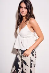 Blusa blanca de algodón con tirantes finos, escote en V con detalles de encaje y pliegues, y un bajo con volantes.