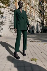 Blazer cruzado de color verde oscuro, con cuello de solapa, manga larga, bolsillos delanteros con solapa y cierre frontal con dos botones dorados.