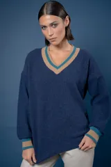 Buzo de punto en lambswool, color azul, con escote en V y detalles de rayas en contraste color beige y turquesa en cuello y puños. Diseño de corte holgado y manga larga.