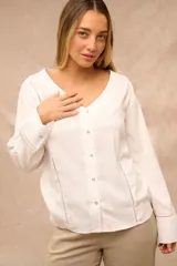 Blusa blanca de manga larga con escote en V y cierre frontal de botones. Presenta detalles de costuras caladas a lo largo del frente y en las mangas.
