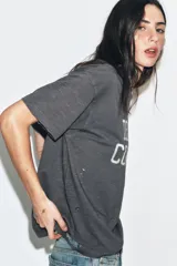 Camiseta de corte oversize confeccionada en algodón flamé, con cuello redondo y manga corta. Presenta un diseño con efecto desgastado, detalles de roturas en el tejido y estampado de texto a contraste en la parte frontal.