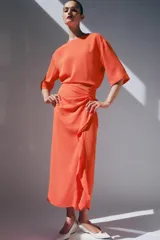 Vestido midi color naranja de la colección ZW de Zara, con cuello redondo, manga corta y detalle de tejido drapeado con volados en el delantero. Cuenta con cierre en la espalda con abertura y botón.