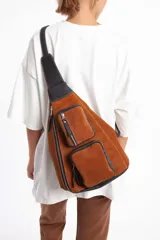 Bolso bandolera de cuero gamuzado color marrón con detalles en cuero negro. Tiene correa regulable, cierre principal y dos bolsillos frontales con cierre.