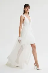 Vestido corto de color blanco con escote en V pronunciado, detalles de encaje en el torso y tirantes anchos con apliques. Presenta una falda corta de encaje con diseño recto.