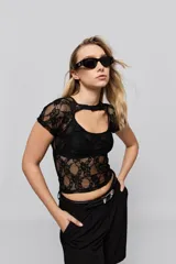 Top de encaje negro con diseño de manga corta, escote redondo y detalle de cut-out en la parte superior del pecho. Presenta un calce ajustado al cuerpo y una textura floral característica del encaje.