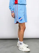 Short deportivo celeste con ribetes rojos y blancos, cintura elástica y escudo del Club Nacional de Football estampado en la pierna izquierda.