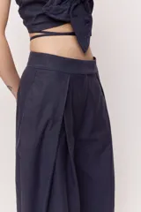 Pantalón azul marino de tiro alto con cintura ancha y pliegues frontales que aportan volumen y una caída suelta y fluida, con diseño envolvente en la cadera y bolsillos laterales.