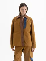 Chaqueta color marrón confeccionada en gabardina, con cuello y cartera de cuero marrón. Presenta broches a tono de cuero en la cartera y puños, bolsillos plaqué y sastreros en el delantero. Incluye volados de denim azul que aportan un toque original al diseño.