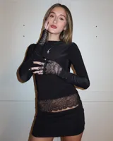 Remera negra de manga larga con cuello redondo, confeccionada en tejido suave con detalles de encaje en el borde inferior y en las mangas.