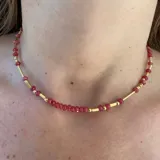 Gargantilla con cuentas facetadas color fucsia y cuentas cilíndricas doradas.