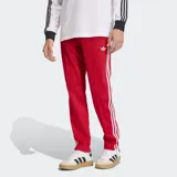 Pantalón deportivo Adidas de corte ajustado, color rojo con las icónicas tres tiras blancas laterales y logo del trébol bordado en la parte superior. Confeccionado en tejido de piqué con cintura elástica y cordón de ajuste.